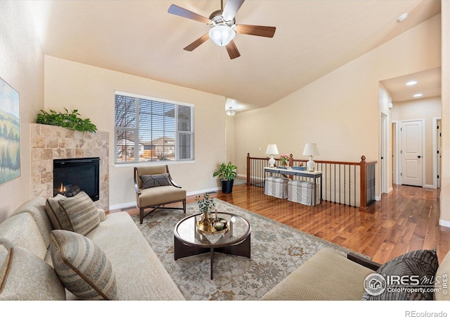 living room with a tile fireplace, hardwood / wood-style flooring, ceiling fan, and vaulted ceiling