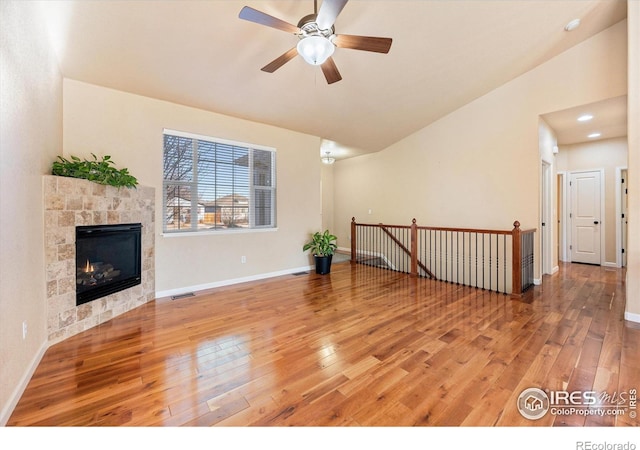 unfurnished living room with a tiled fireplace, ceiling fan, hardwood / wood-style floors, and lofted ceiling