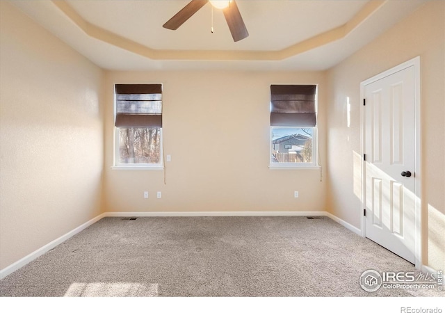 empty room featuring ceiling fan, a tray ceiling, and carpet