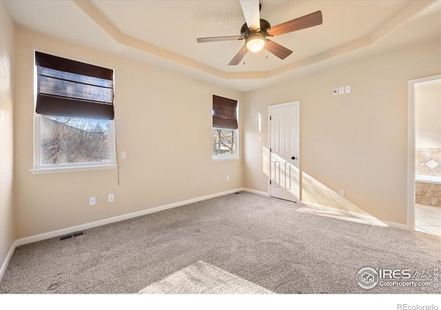 spare room with ceiling fan, light carpet, and a raised ceiling