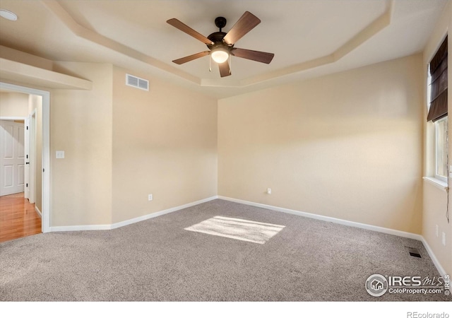 carpeted spare room with ceiling fan and a tray ceiling