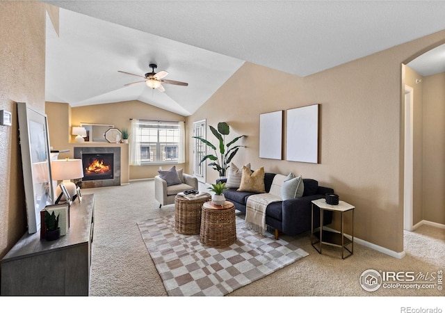 carpeted living room with a tile fireplace, ceiling fan, and vaulted ceiling