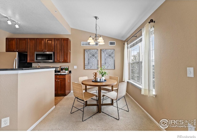 dining area with a chandelier, track lighting, light colored carpet, and vaulted ceiling