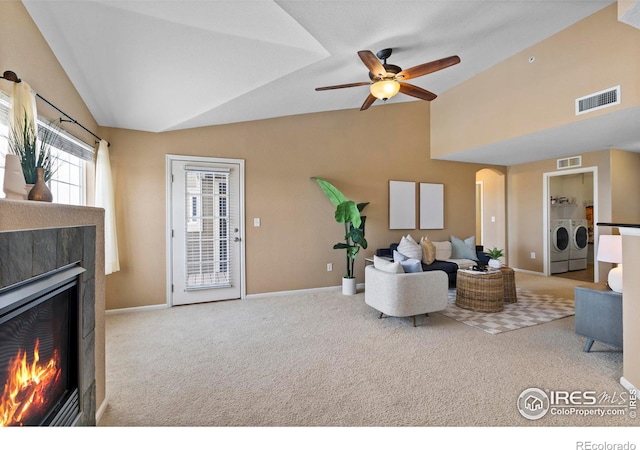 carpeted living room with washer and dryer, ceiling fan, a tile fireplace, and vaulted ceiling