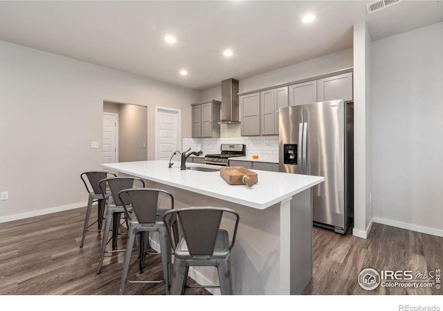 kitchen with sink, stainless steel appliances, wall chimney range hood, a kitchen bar, and a kitchen island with sink