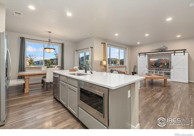 kitchen featuring gray cabinetry, sink, stainless steel appliances, hanging light fixtures, and an island with sink