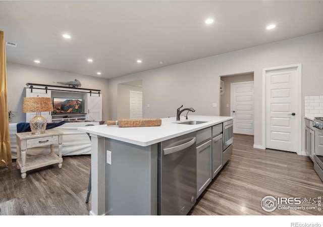 kitchen featuring hardwood / wood-style floors, a kitchen island with sink, sink, gray cabinets, and stainless steel appliances