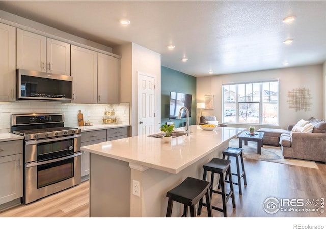 kitchen with appliances with stainless steel finishes, a kitchen breakfast bar, gray cabinetry, sink, and an island with sink