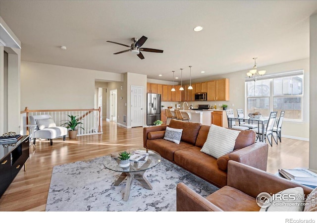 living room featuring ceiling fan with notable chandelier, light hardwood / wood-style floors, and sink