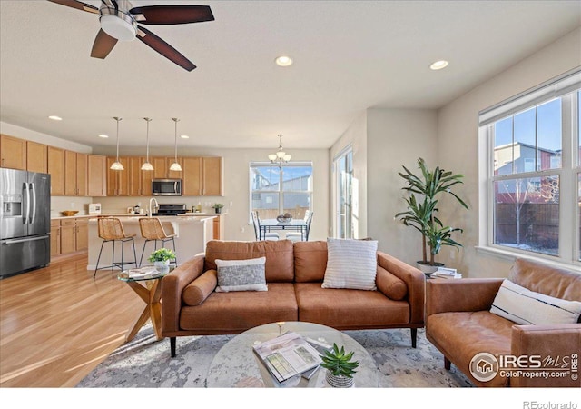 living room with ceiling fan with notable chandelier and light wood-type flooring