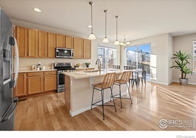 kitchen with a center island with sink, sink, appliances with stainless steel finishes, decorative light fixtures, and a chandelier