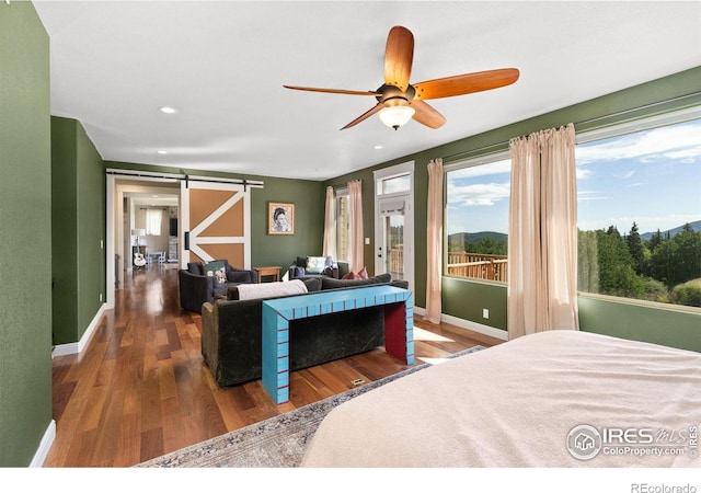 bedroom with ceiling fan, a barn door, and dark wood-type flooring