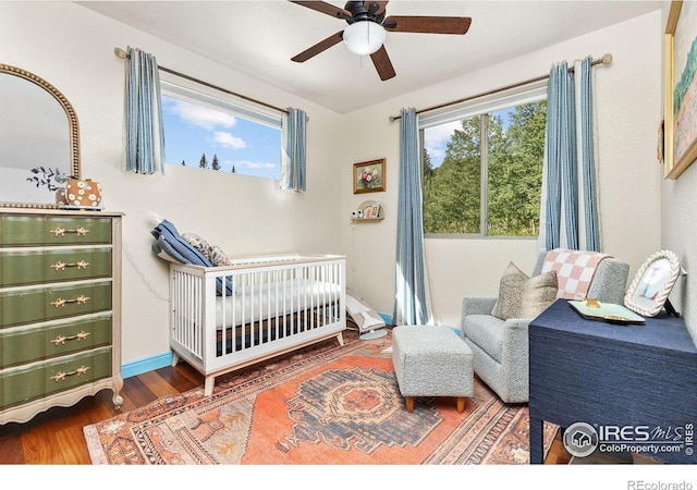 bedroom with ceiling fan, hardwood / wood-style floors, and a nursery area