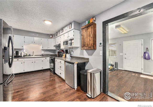 kitchen with appliances with stainless steel finishes, a textured ceiling, dark wood-type flooring, sink, and white cabinets