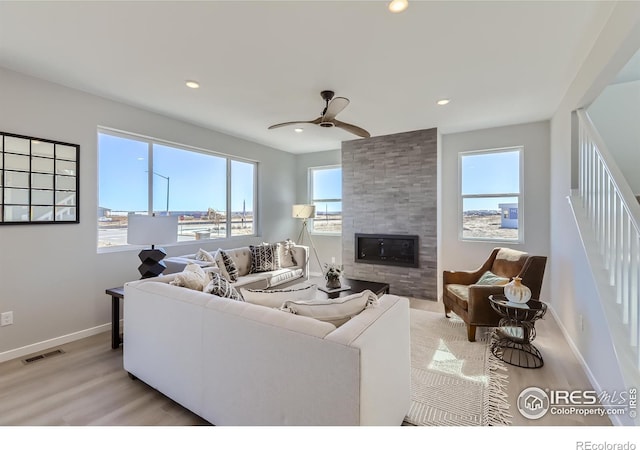 living room with ceiling fan, a large fireplace, and light hardwood / wood-style flooring