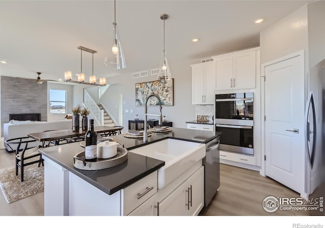 kitchen featuring a kitchen island with sink, white cabinets, stainless steel appliances, and decorative light fixtures