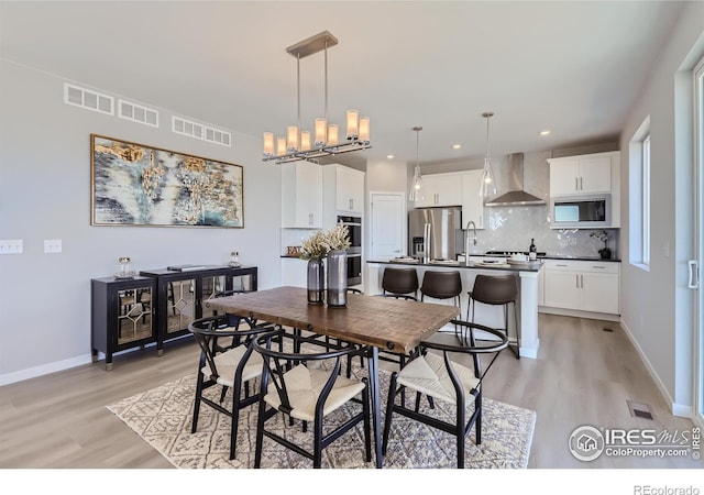 dining area with light wood-type flooring, an inviting chandelier, and sink