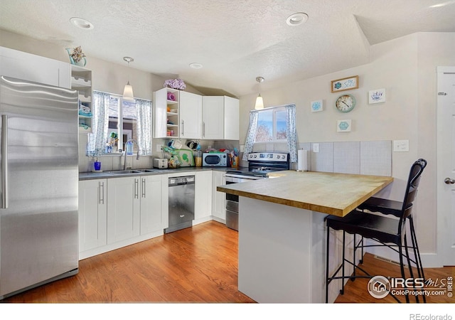 kitchen with kitchen peninsula, appliances with stainless steel finishes, a kitchen breakfast bar, sink, and white cabinets