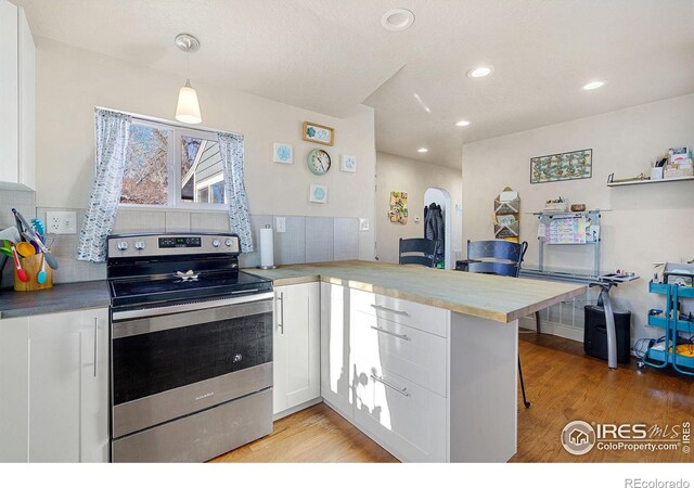 kitchen featuring hanging light fixtures, stainless steel range with electric cooktop, kitchen peninsula, a kitchen bar, and white cabinets