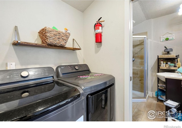 clothes washing area featuring washer and clothes dryer, light wood-type flooring, and a textured ceiling