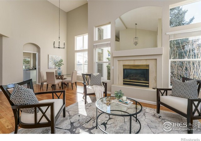 living room featuring an inviting chandelier, high vaulted ceiling, a high end fireplace, and light hardwood / wood-style floors