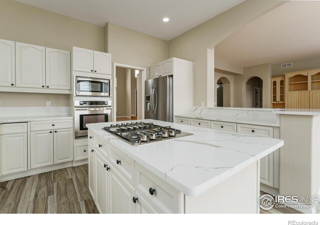 kitchen with a kitchen island, white cabinetry, light stone counters, stainless steel appliances, and dark wood-type flooring