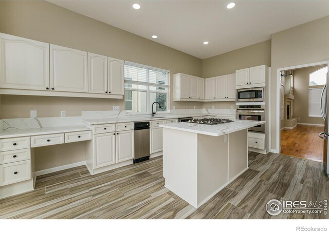 kitchen featuring appliances with stainless steel finishes, white cabinetry, light stone counters, a wealth of natural light, and a kitchen island