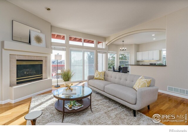 living room featuring a tiled fireplace, a chandelier, and light hardwood / wood-style floors