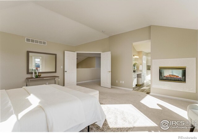 carpeted bedroom featuring vaulted ceiling, a multi sided fireplace, and ensuite bathroom