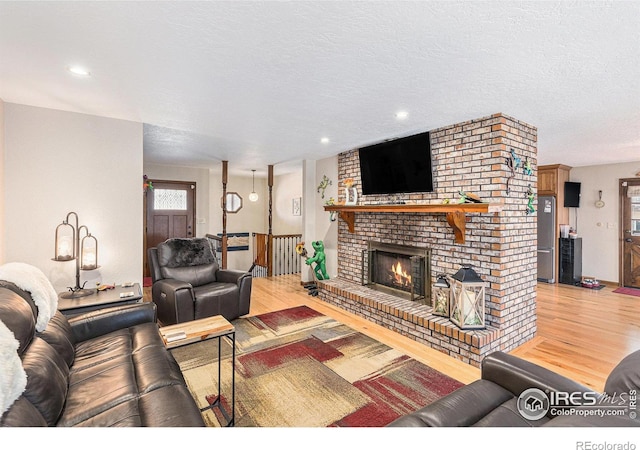 living room featuring light hardwood / wood-style flooring, a textured ceiling, and a brick fireplace