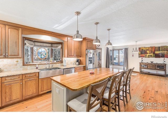 kitchen with stainless steel appliances, sink, a kitchen island, hanging light fixtures, and butcher block counters