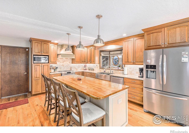 kitchen featuring pendant lighting, a center island, sink, butcher block countertops, and stainless steel appliances