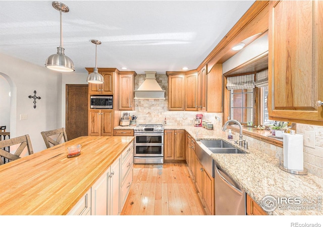 kitchen featuring custom exhaust hood, wood counters, sink, tasteful backsplash, and stainless steel appliances