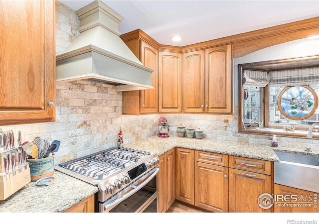 kitchen with light stone countertops, custom range hood, backsplash, and range with two ovens