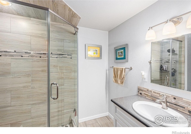 bathroom featuring vanity, a shower with shower door, and backsplash