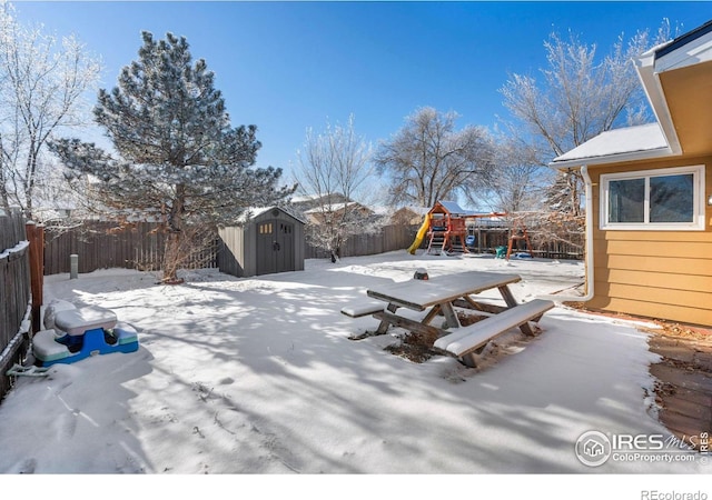 yard layered in snow with a playground and a storage unit