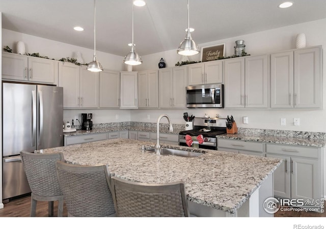 kitchen featuring light stone countertops, sink, stainless steel appliances, pendant lighting, and a center island with sink