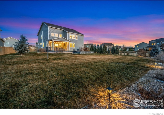 back house at dusk featuring a lawn and a patio area