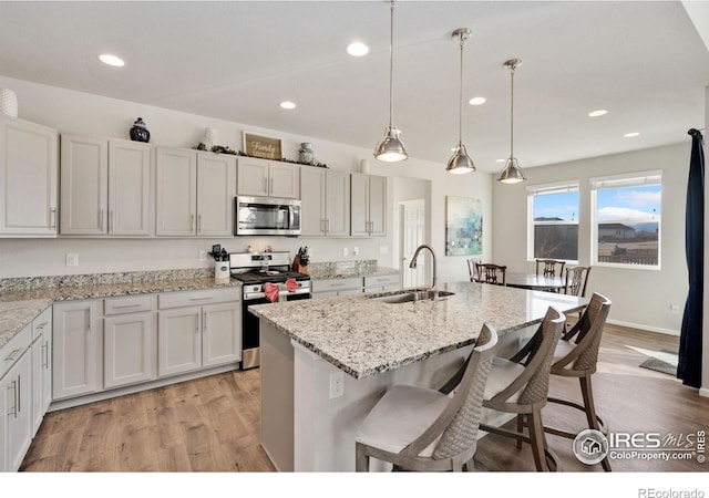 kitchen with a kitchen island with sink, sink, appliances with stainless steel finishes, decorative light fixtures, and light hardwood / wood-style floors