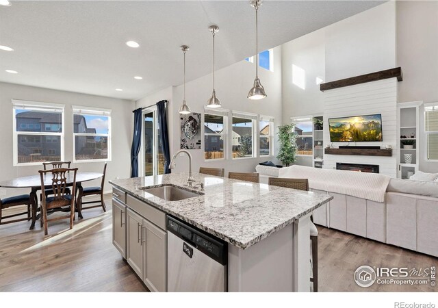 kitchen featuring dishwasher, a kitchen island with sink, sink, a fireplace, and decorative light fixtures