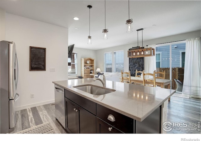 kitchen with stainless steel appliances, sink, pendant lighting, a center island with sink, and light hardwood / wood-style floors