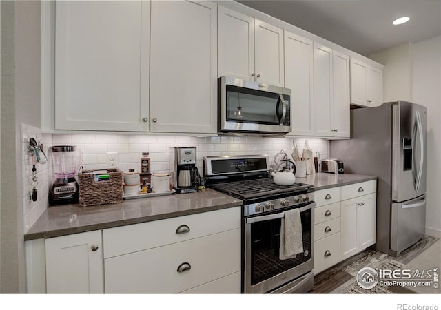 kitchen featuring white cabinetry, dark wood-type flooring, tasteful backsplash, dark stone counters, and appliances with stainless steel finishes