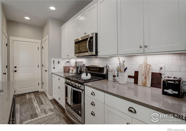 kitchen featuring light stone countertops, backsplash, stainless steel appliances, dark wood-type flooring, and white cabinetry