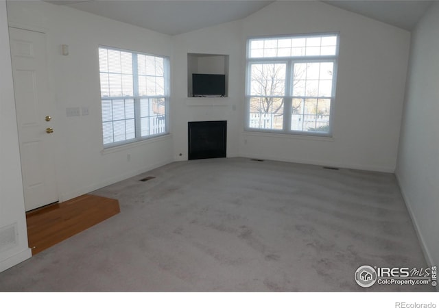 unfurnished living room featuring plenty of natural light, lofted ceiling, and light carpet