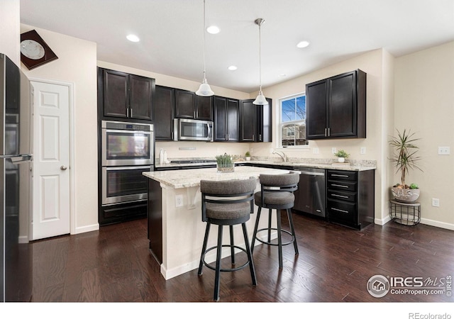 kitchen with pendant lighting, dark wood-style flooring, appliances with stainless steel finishes, a kitchen island, and light stone countertops