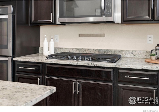 kitchen featuring stainless steel appliances, dark brown cabinets, and light stone counters