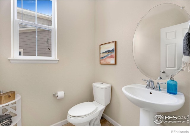 half bathroom featuring toilet, baseboards, and a sink