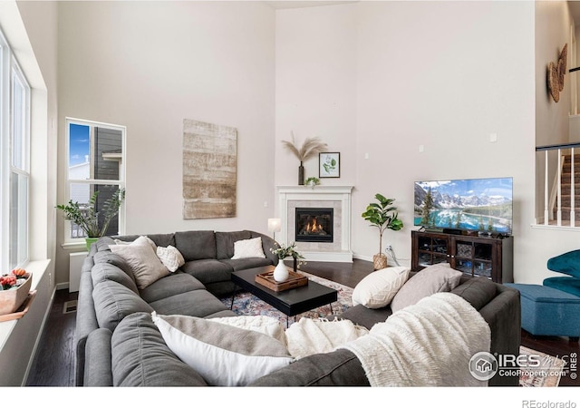 living area with a towering ceiling, visible vents, dark wood-type flooring, and a glass covered fireplace