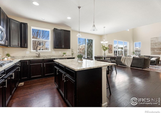 kitchen featuring a sink, a kitchen island, open floor plan, hanging light fixtures, and dark wood finished floors