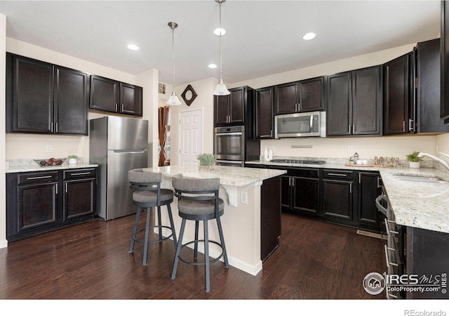 kitchen with light stone counters, stainless steel appliances, a sink, a kitchen island, and pendant lighting